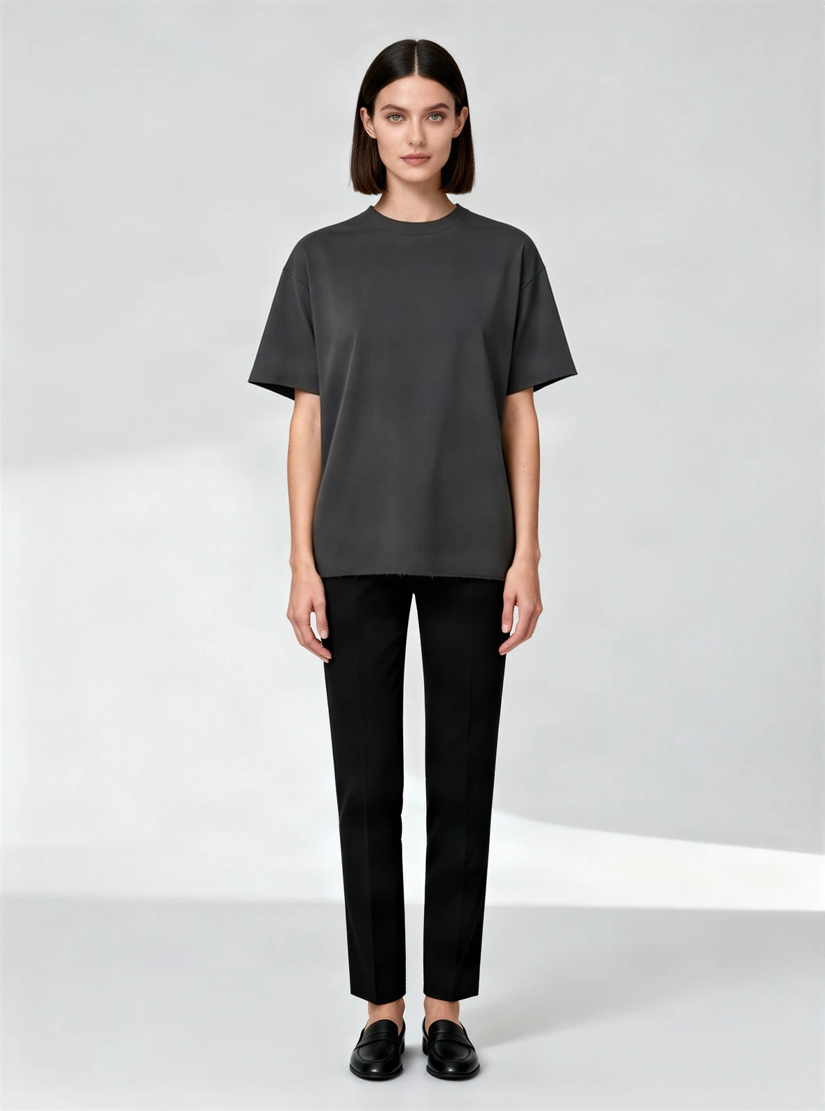 AI fashion model wearing the charcoal T-shirt, standing in a light studio - AI-generated model